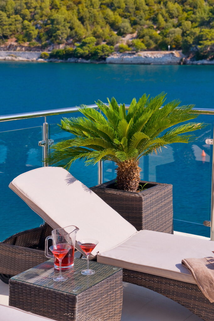 A sunbed with a white pillow, and two glasses of rose wine on the balcony with a direct sea view.