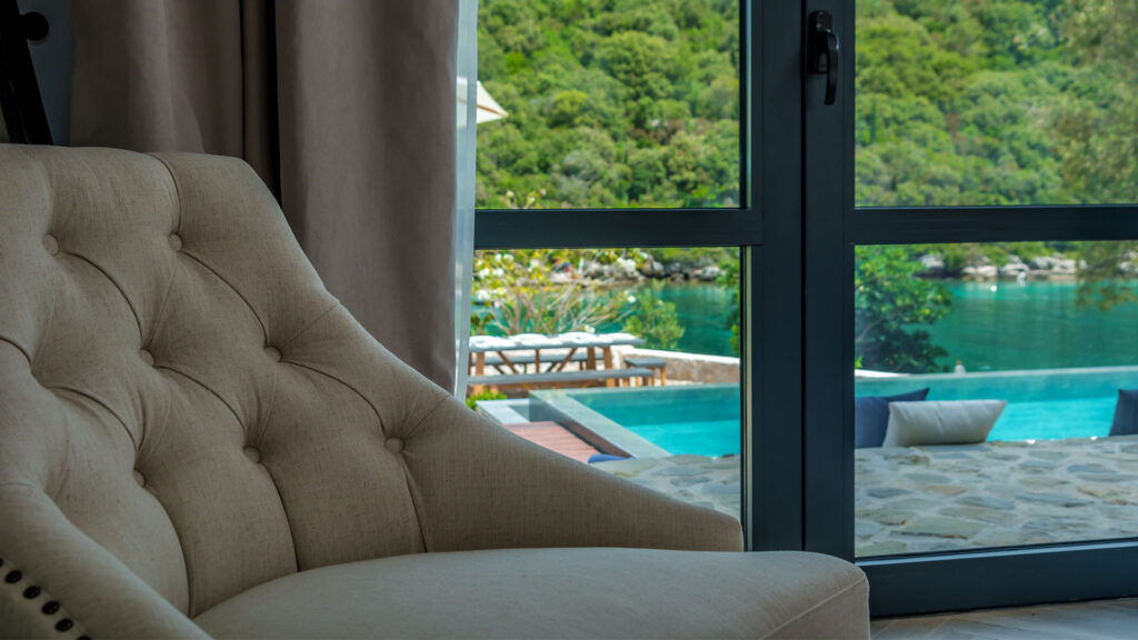 The white chair in front of the glass doors which have the view on the garden with a pool.